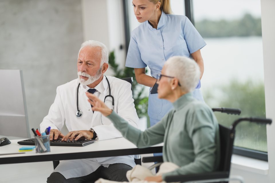 Doctor and nurse speaking with an older patient in a wheelchair at a clinic
